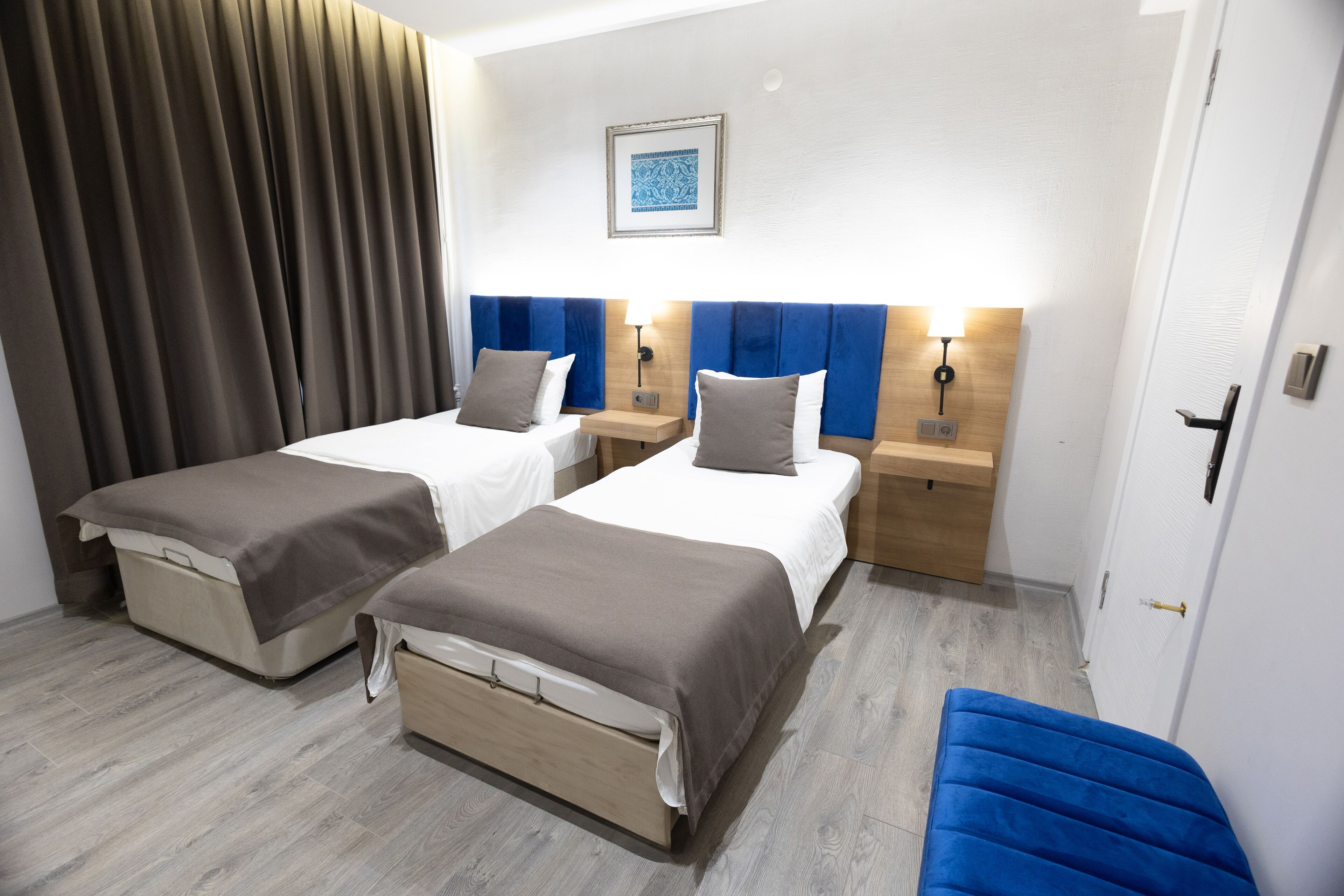 Ein Hotelzimmer mit zwei Betten, einer blauen Bank, einem hölzernen Nachttisch und einer Wandlampe.