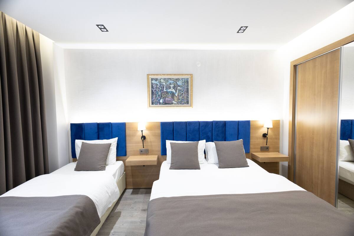 A hotel room with two beds, a large mirror, a painting on the wall, and a wooden headboard.