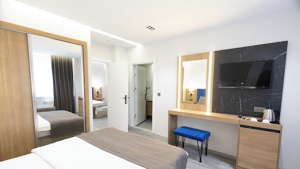A hotel room with a bed, a desk with a TV, a mirror, and a bathroom visible through an open door.