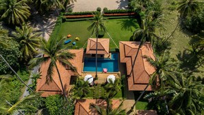 Vista aérea de un resort con piscina, palmeras y una playa.