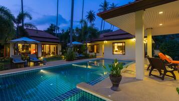 Relax by the serene pool surrounded by lush greenery and lounge chairs under umbrellas.