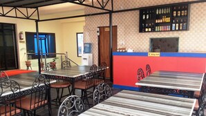 A restaurant with multiple tables and chairs, a kitchen area, and a water dispenser. - Hotel Crown (Tansen)