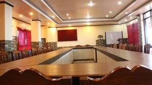 A conference room with a long table and chairs, recessed ceiling lights, and a red curtain. - Hotel Crown (Tansen)
