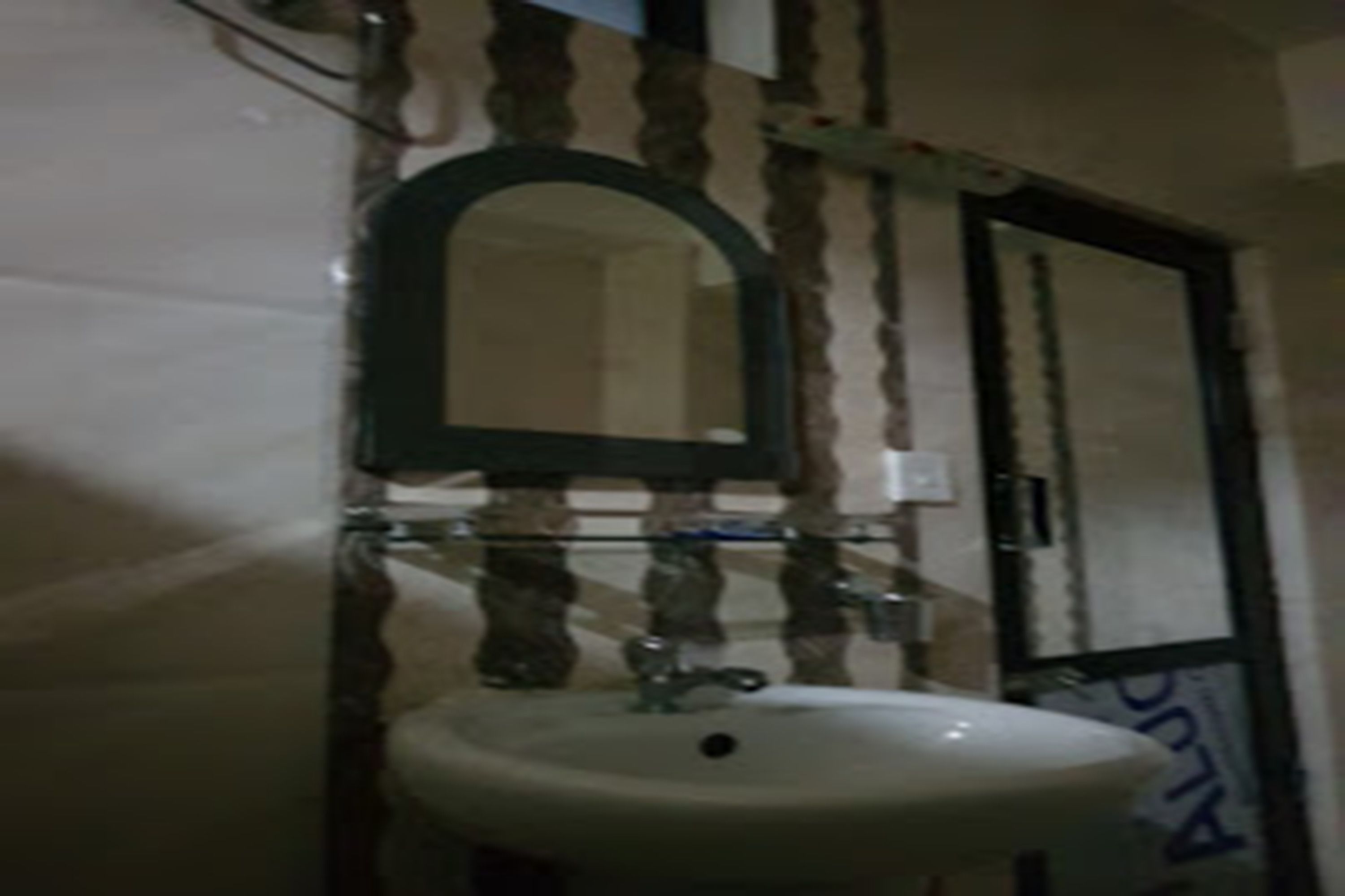 Un baño con lavamanos blanco, un espejo encima y una puerta con marco negro.