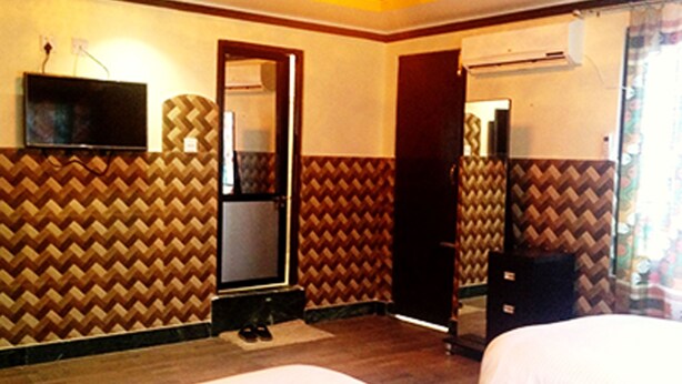A hotel room with a bed, a TV, a mirror, and a wardrobe. - Hotel Crown (Tansen)