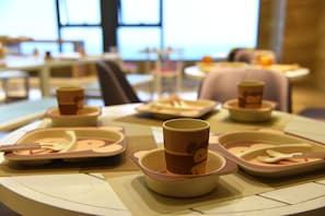 Un comedor con mesas redondas, cada una con una taza, cuchara y tenedor colocados en recipientes a juego.