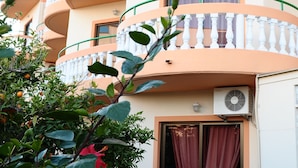 A multi-story building with balconies, air conditioning units, and a window with curtains. - Villa George Studios (Rhodes)