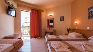 A hotel room with two beds, a desk, a chair, a TV, and a balcony with a red curtain. - Villa George Studios (Rhodes)
