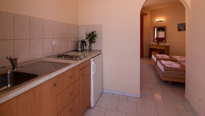 A compact kitchen with a sink, stove, and dishwasher, leading to a small bathroom with a mirror and towel rack. - Villa George Studios (Rhodes)