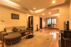 A living room with a sofa, coffee table, and TV stand. There is a dining area with chairs and a table.