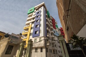 Un immeuble à plusieurs étages doté de balcons, d’une entrée sécurisée et d’une enseigne indiquant la présence d’un commerce au rez-de-chaussée.