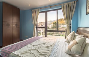 A bedroom with a large bed, a wardrobe, and a balcony with a city view.
