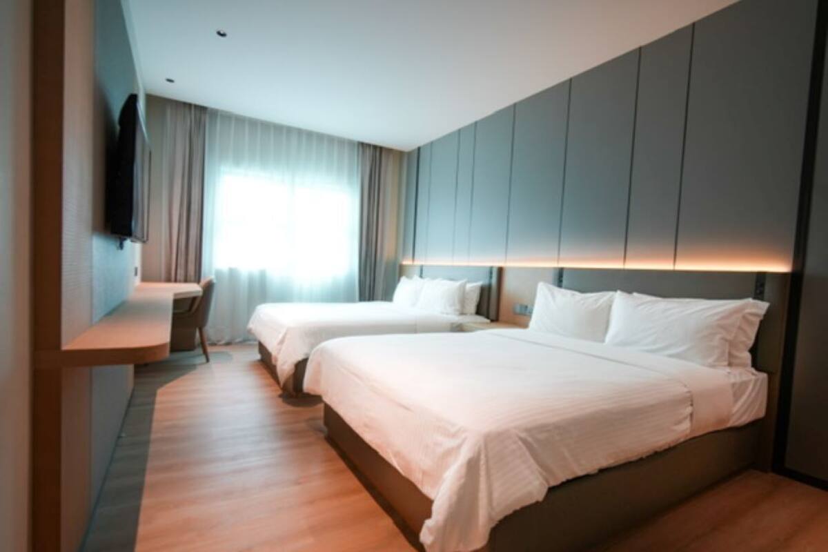 A modern hotel room with two beds, a desk, and a TV.