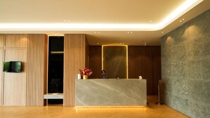 Un espace d’accueil moderne doté d’un comptoir en marbre, de panneaux muraux en bois et d’un téléviseur à écran plat fixé au mur.