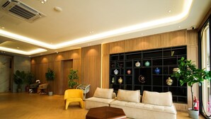 Un salon moderne avec un canapé, un fauteuil jaune et une table basse en bois. Un mur est décoré d’étagères où sont exposés des objets décoratifs.