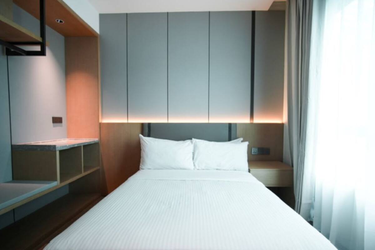 A modern hotel room with a large bed, built-in headboard, and a bedside table.