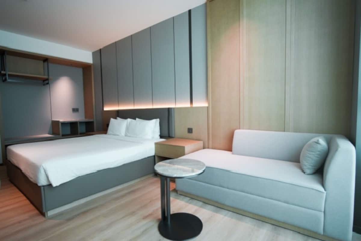 A modern hotel room with a bed, a sofa, a small round table, and built-in cabinets.