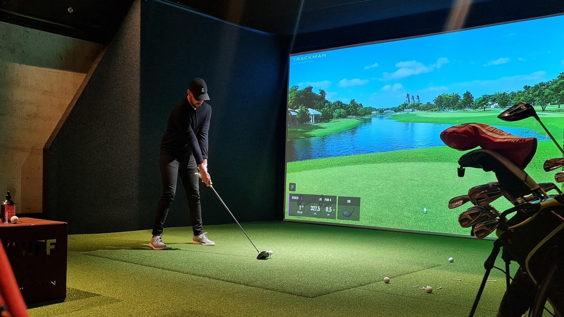 A person practicing golf in a room with a large screen displaying a golf course.