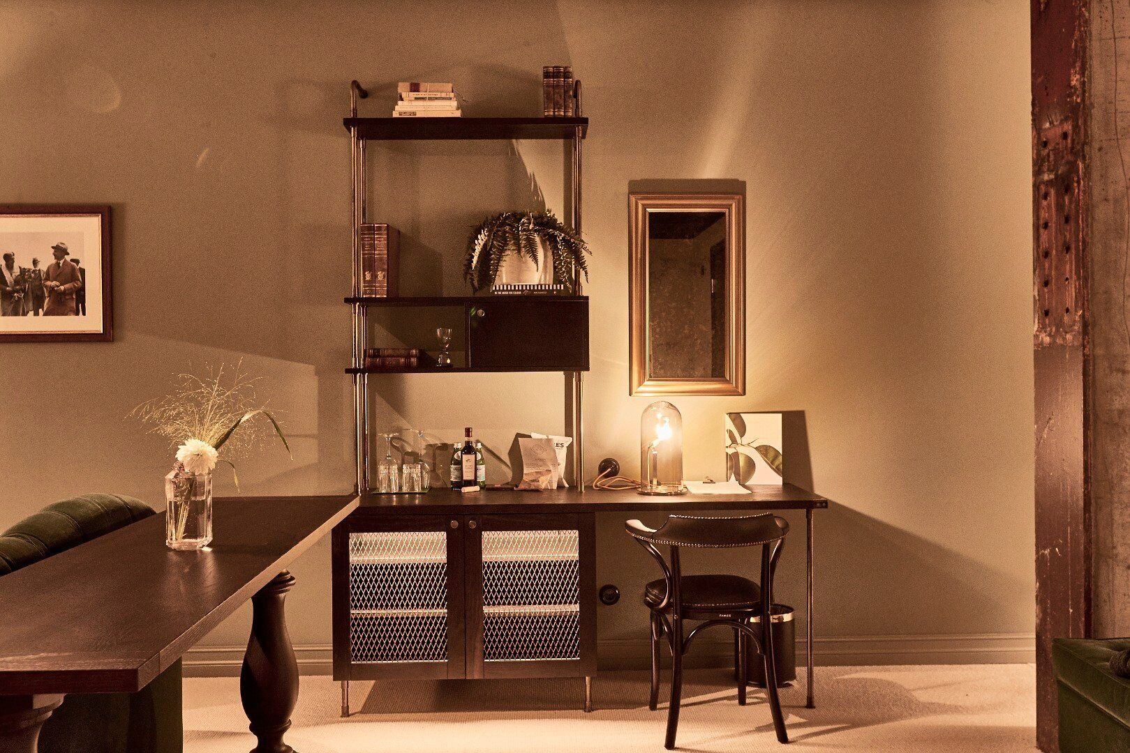 A room with a dark wooden desk, a chair, a bookshelf, a framed picture, and a vase with flowers.