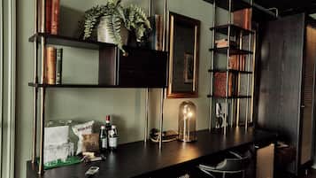 Zona de bar con mostrador de madera, estanterías con libros y objetos decorativos, una planta colgante e iluminación colgante.
