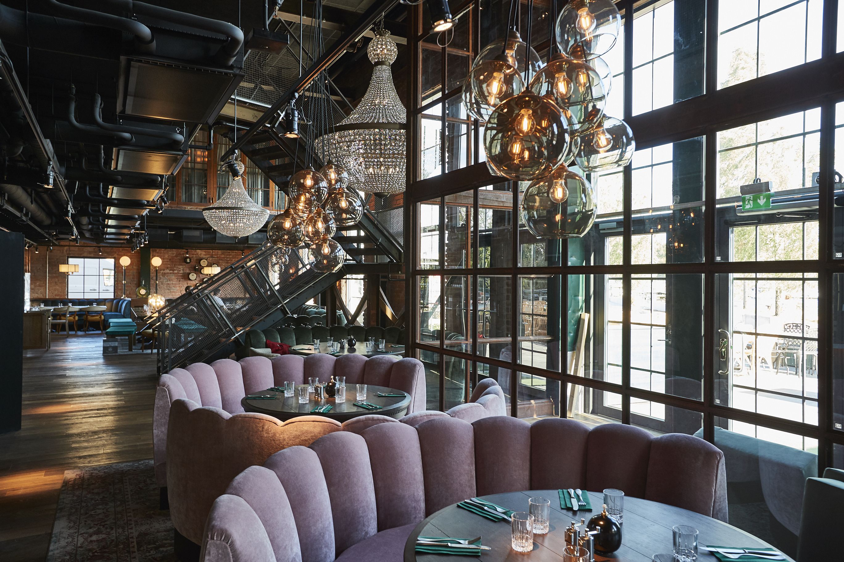 Un restaurante con mesas redondas, asientos acolchados y lámparas colgantes.