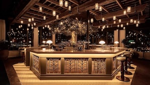A bar area with a central island, multiple hanging lights, and a view of the cityscape through large windows.