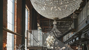 A spacious interior with a large chandelier, wooden floors, and a staircase leading to an upper level.