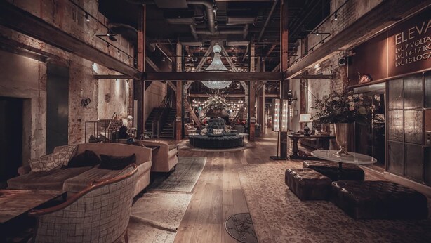 A spacious lobby with a central seating area, wooden floors, and exposed brick walls.