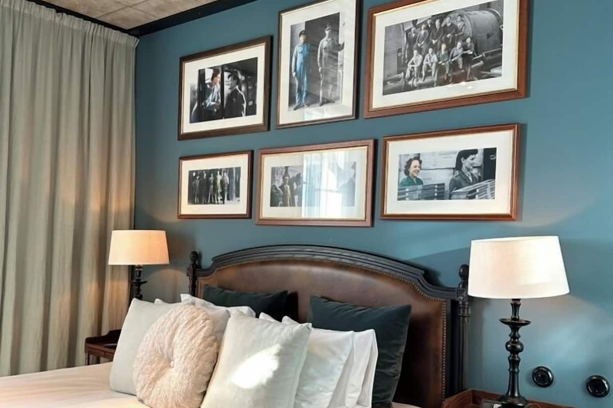 Un dormitorio con una cama grande, dos mesitas de noche con lámparas, un cabecero de madera y una pared decorada con fotografías enmarcadas.