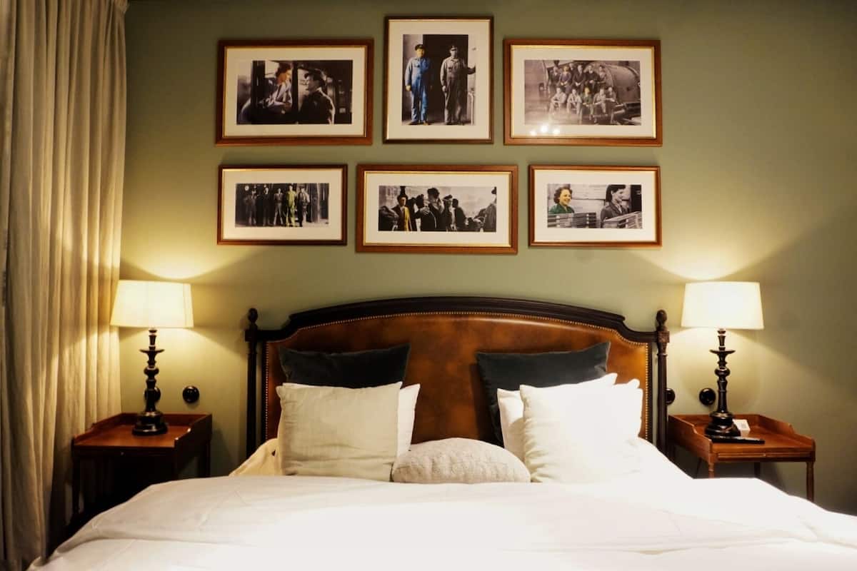 Una habitación de hotel con una cama grande, dos mesitas de noche con lámparas, y seis fotografías enmarcadas en la pared.