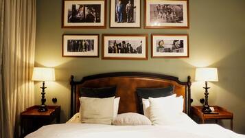 Una habitación de hotel con una cama grande, dos mesitas de noche con lámparas, y seis fotografías enmarcadas en la pared.