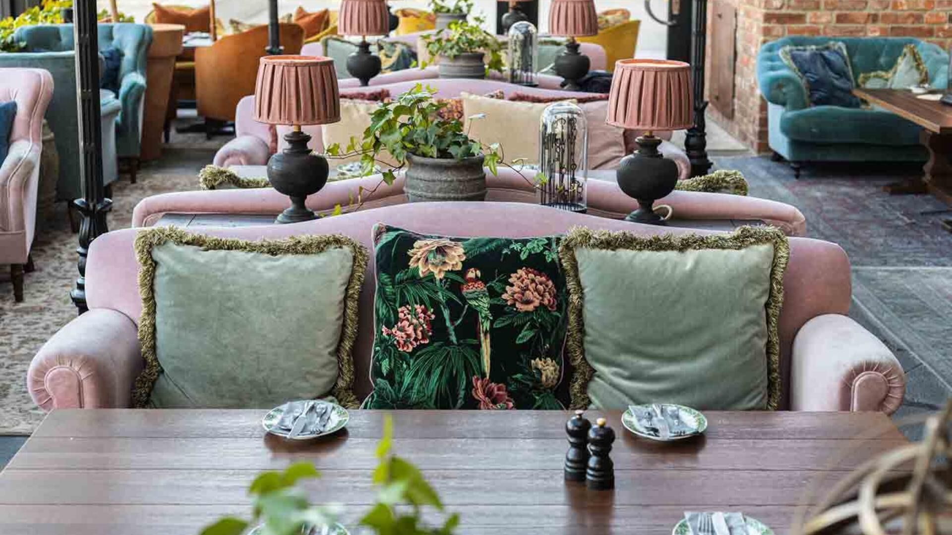 A cozy seating area with plush sofas and armchairs, a wooden table with plates and cutlery, and decorative lamps.