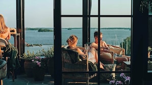 A cozy outdoor seating area with wicker furniture and potted plants, overlooking a body of water.