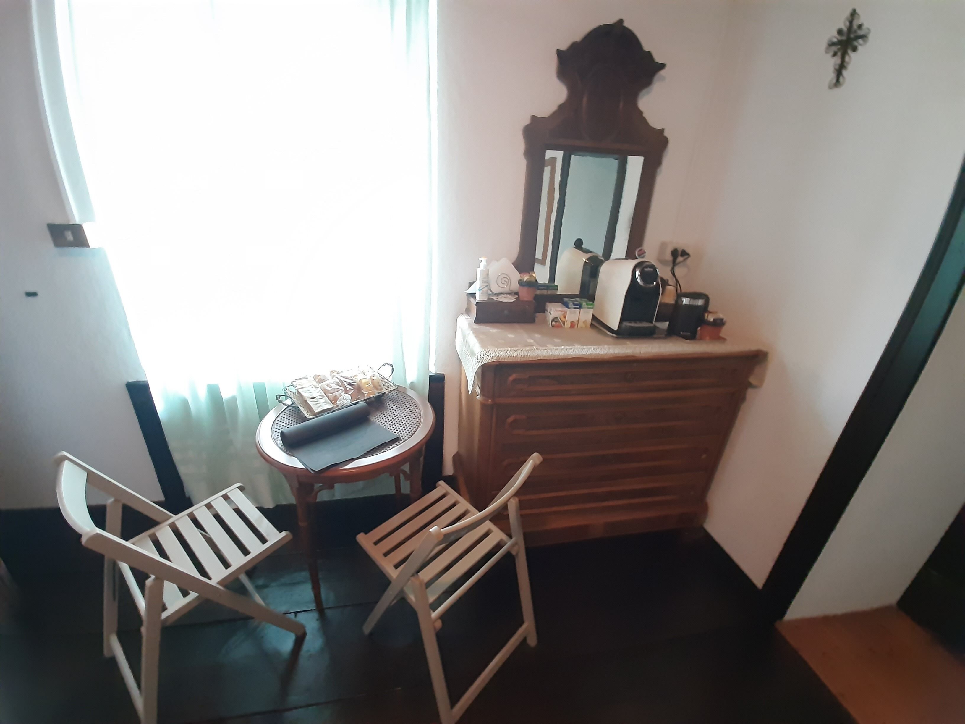 A small room with a wooden dresser, a mirror, a table with a tray of items, and two chairs.