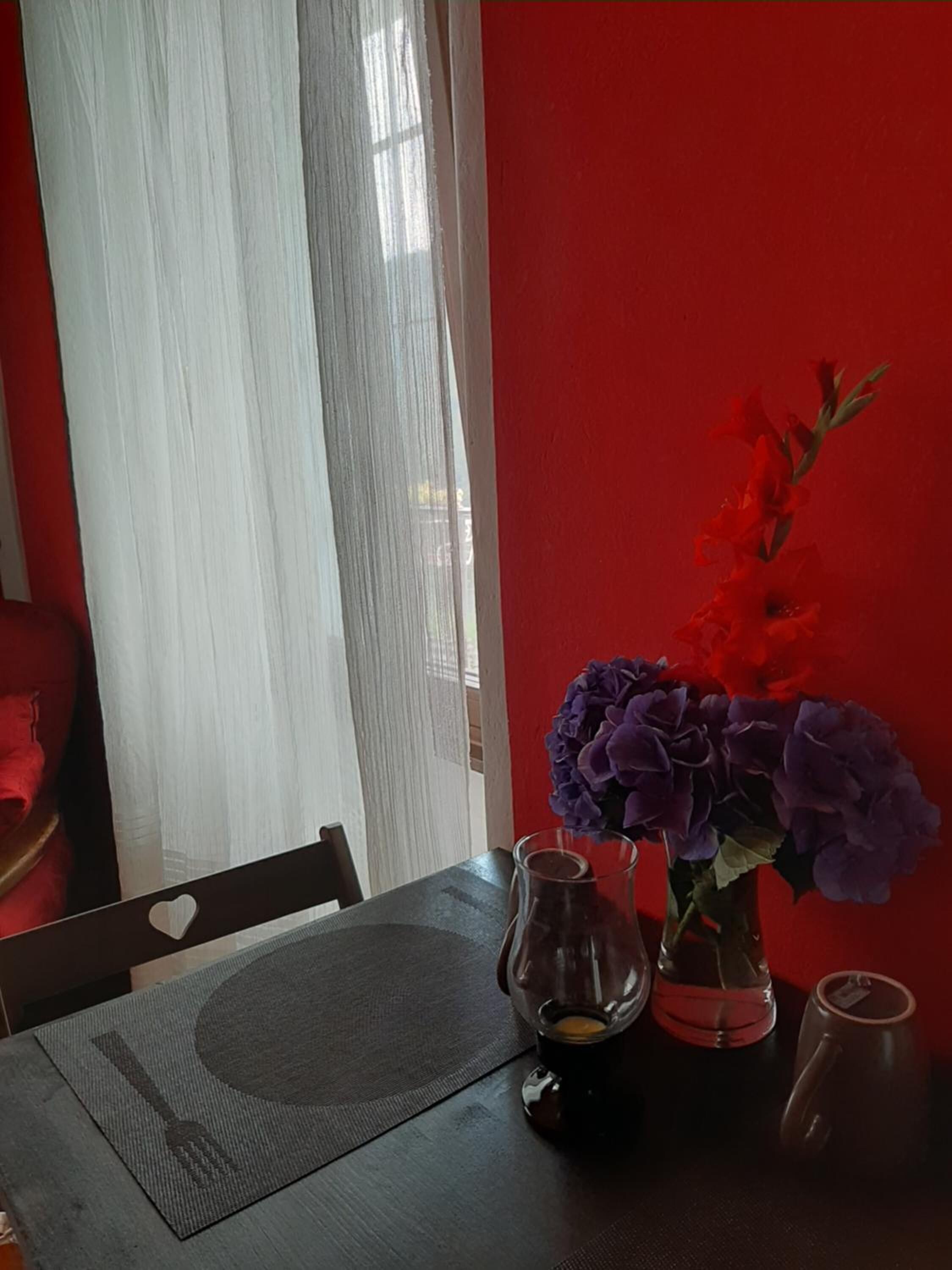 Una mesa de comedor con un mantel individual, un jarrón con flores moradas, una jarra de vidrio y una taza.