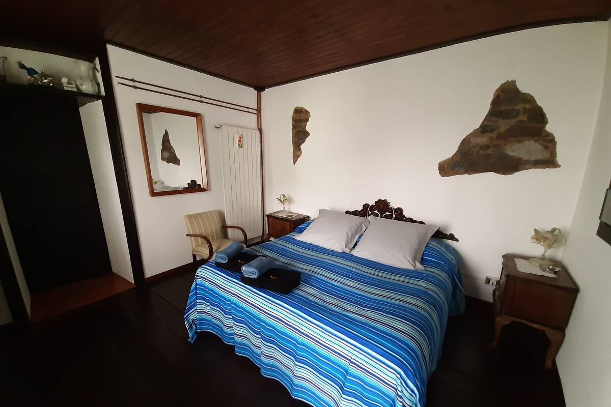 A bedroom with a bed, a chair, a nightstand, and a wall with a rock-like decoration.