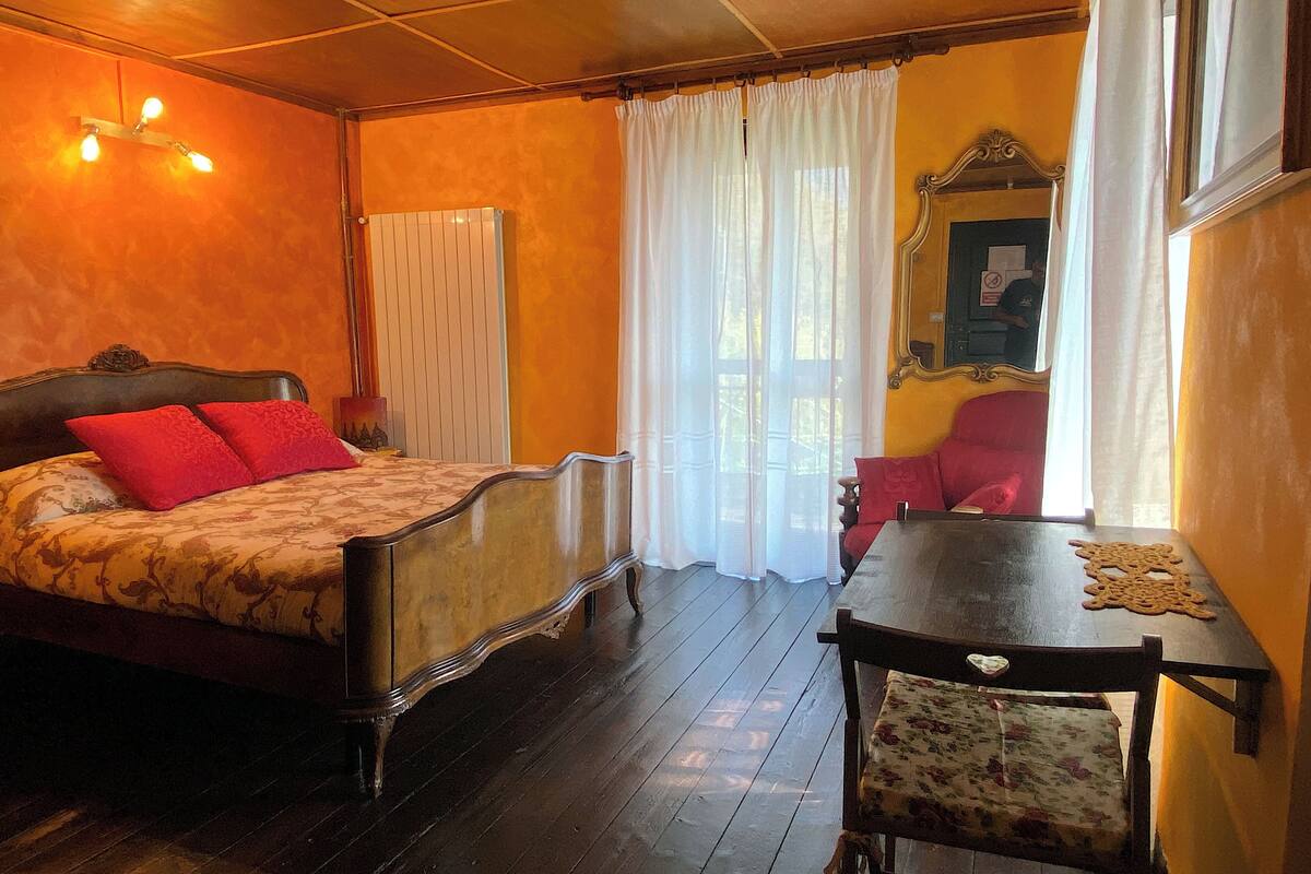 A room with a bed, a table, a chair, a window with curtains, and a radiator.