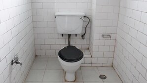 A small, white-tiled bathroom with a white toilet and a black seat. - Hotel New Dragon (Baluwapati Deupur)