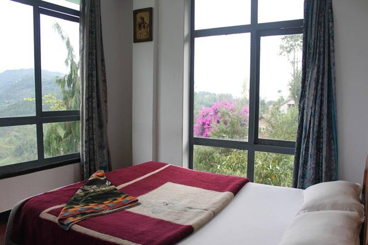 Quarto com cama, janela com vista para vegetação e montanhas, e quadro na parede.