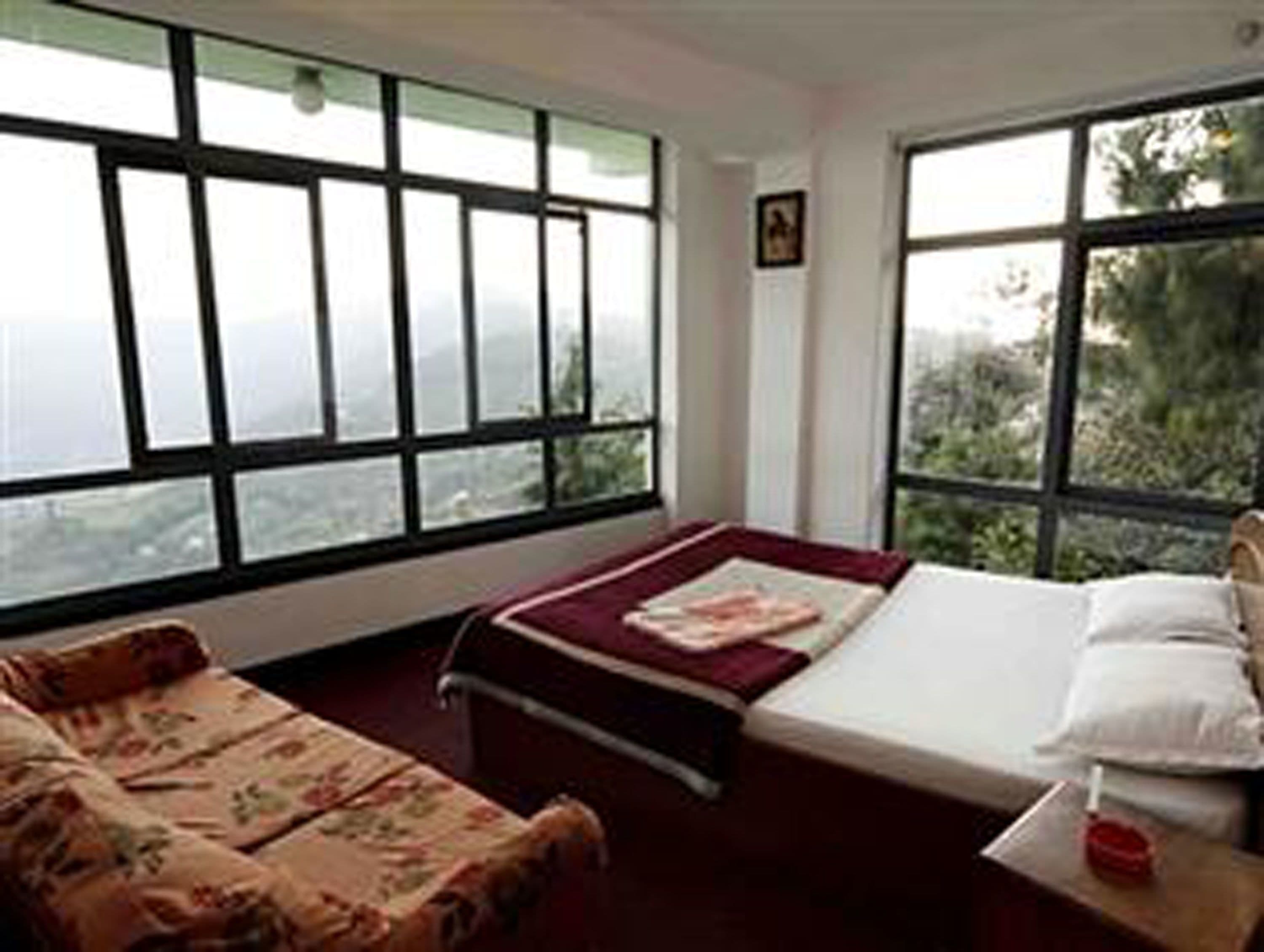 A room with a bed, a sofa, and large windows offering a view of the outdoors.