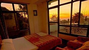 A room with a bed, a window with a view of the sunset, and a chair. - Hotel New Dragon (Baluwapati Deupur)