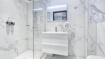 A modern bathroom with a glass-enclosed shower, a white vanity with a mirror, and marble-patterned walls.