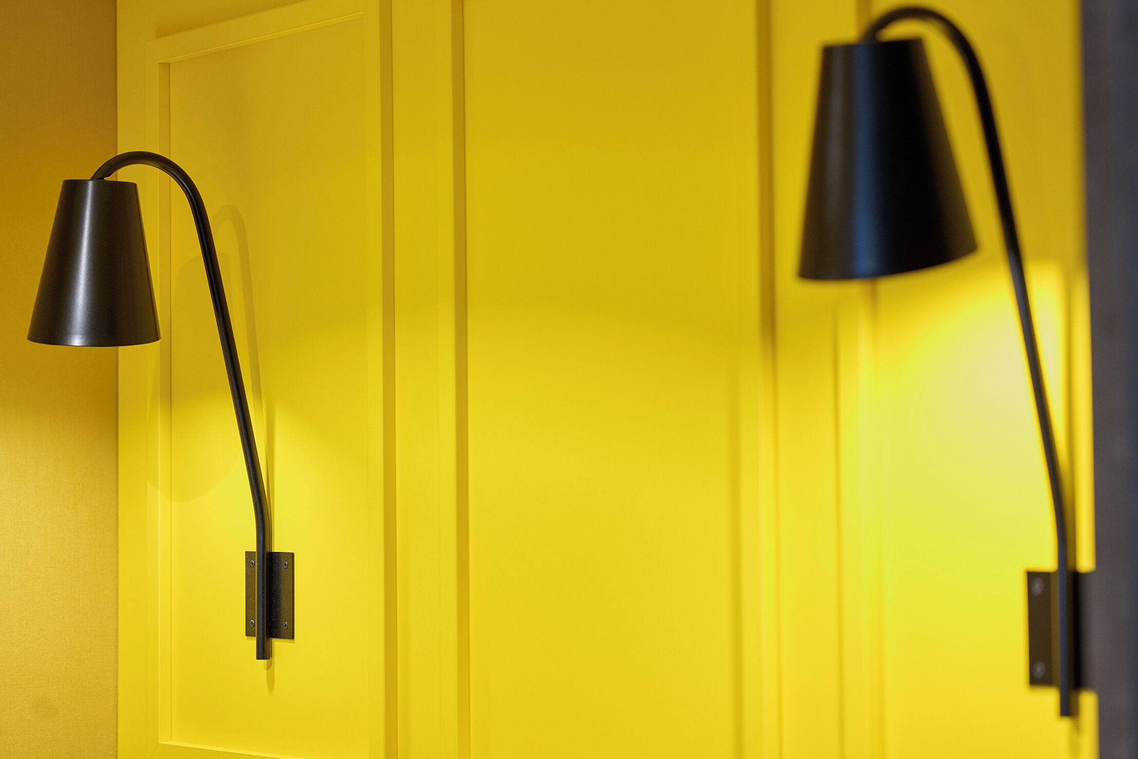 Two black wall-mounted lamps against a yellow door.