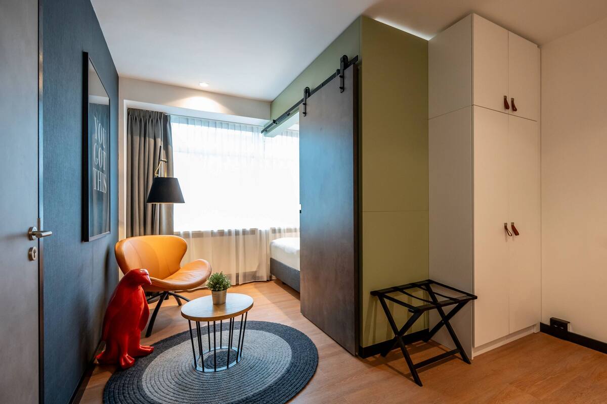 Een moderne kamer met een bed, een stoel, een klein tafeltje en een rode sculptuur.