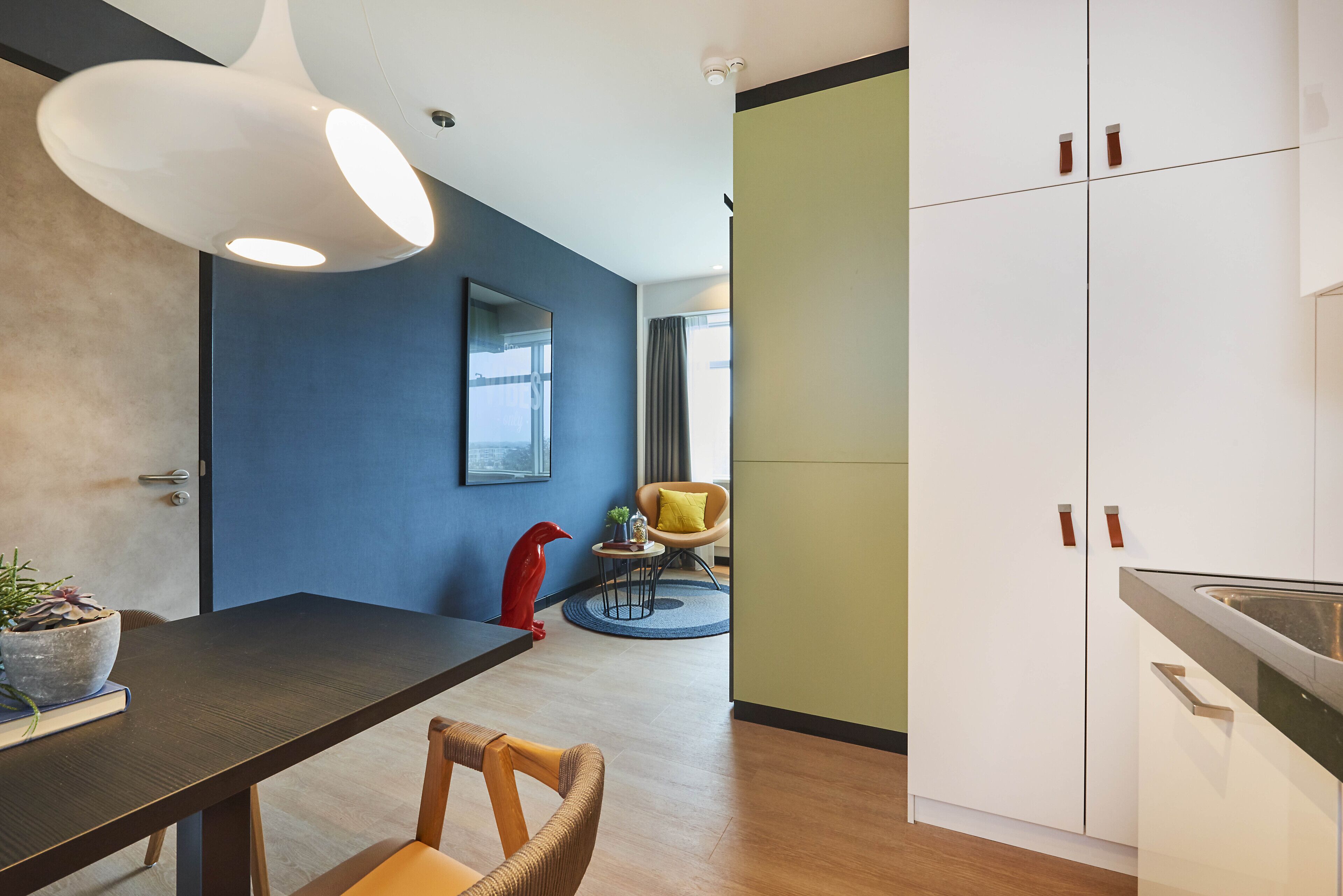 Una cocina moderna con armarios blancos, una zona de comedor con una mesa de madera oscura y una pared de acento azul.