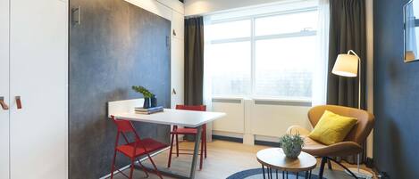 A modern room with a white table, red chairs, a round coffee table, a yellow pillow, and a lamp.