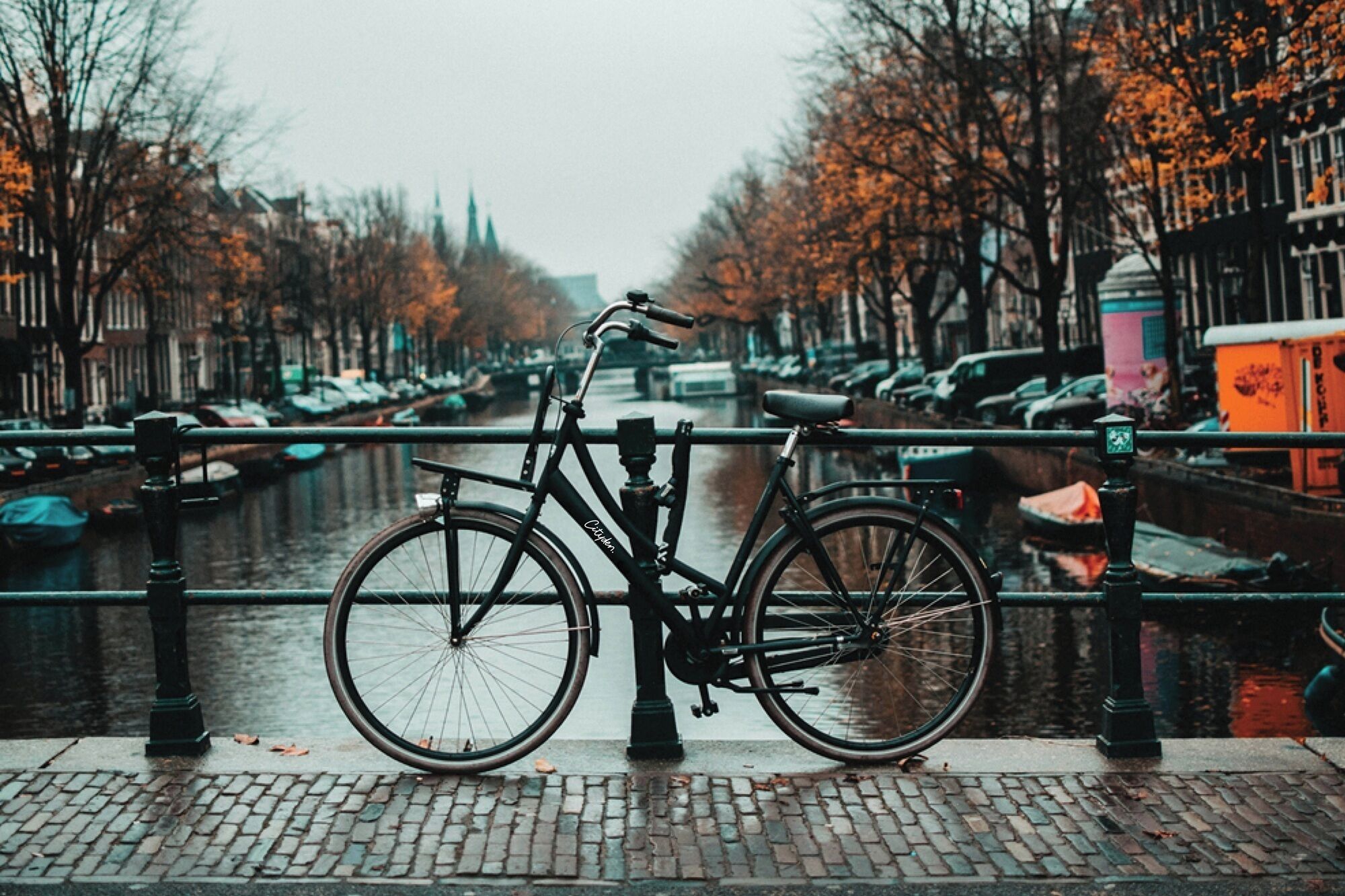 Un vélo est garé au bord d’un canal, avec un pont en arrière-plan.