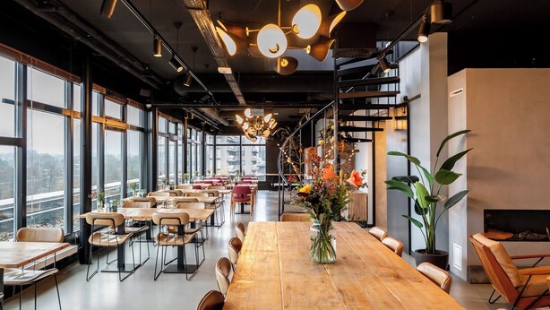 Une salle à manger spacieuse avec de hauts plafonds, un éclairage moderne suspendu et de grandes fenêtres offrant une vue sur la ville.