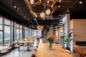 Un comedor espacioso con techos altos, iluminación colgante moderna y ventanas grandes con vistas a la ciudad.