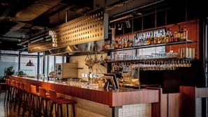 Un espace bar doté d’un long comptoir, de nombreux tabourets et d’étagères remplies de bouteilles et de verres.